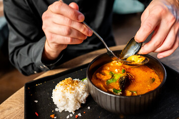 A person enjoying a bowl of seafood soup with rice on the side