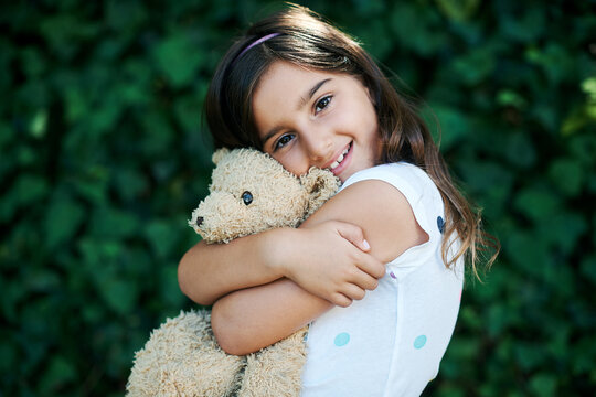 Toys, portrait and girl hug teddy bear outdoor with safety and security in home and garden. Calm, kid or child relax with smile on face or embrace soft doll in backyard with happiness in kindergarten