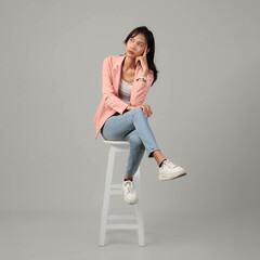 full lenght shoot of pensive asian woman sitting on stool. isolated background