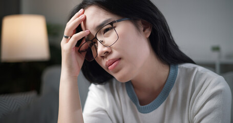 Selective focus, Unwell young woman massaging temples to relieve headache while sitting on sofa at...