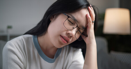 Selective focus, Unwell young woman massaging temples to relieve headache while sitting on sofa at home, healthcare woes