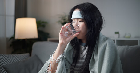 Portrait of Unwell young woman was drinking water, wrapped in blanket sitting on sofa in the living...