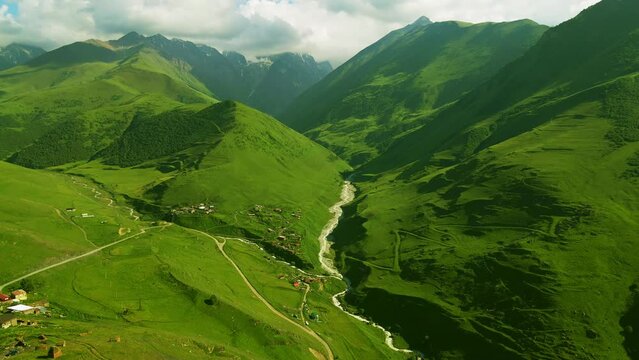 Mountain gorge with river at sunny day. Mountains and hills with fresh green grass. Aerial view. Summer landscape. Digor Gorge in North Ossetia, Caucasus, Russia. 