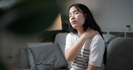 Portrait of Unwell young woman has neck pain while sitting on the sofa in the living room. People...