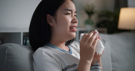 Portrait of Unwell young woman having a cold, sneezing and blowing your nose while sitting on sofa in the living room at home, healthcare woes