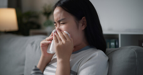 Portrait of Unwell young woman having a cold, sneezing and blowing your nose while sitting on sofa in the living room at home, healthcare woes