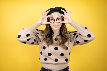 Young beautiful brunette woman wearing french beret and glasses over yellow background Trying to...