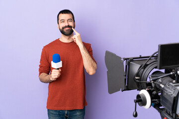 Reporter man holding a microphone and reporting news over isolated purple background smiling with a happy and pleasant expression