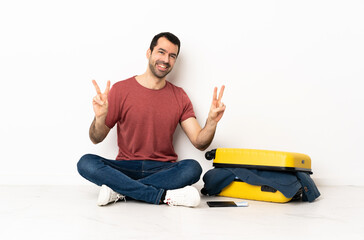 Caucasian handsome man with a suitcase full of clothes sitting on the floor at indoors showing victory sign with both hands