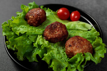 Fried cutlets on a lettuce leaf with tomato on a black background