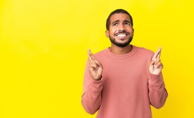 Young latin man isolated on yellow background with fingers crossing and wishing the best