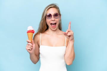 Young blonde woman in swimsuit holding an ice cream isolated on blue background pointing up a great...