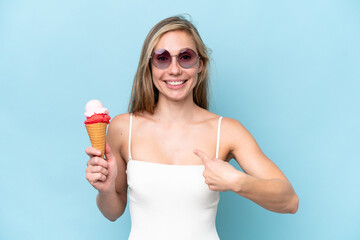 Young blonde woman in swimsuit holding an ice cream isolated on blue background with surprise...