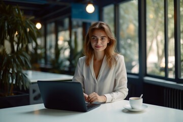 Smiling businesswoman standing at desk with cup of coffee and typing business report on a laptop computer keyboard