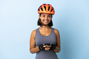 Young cyclist woman isolated on blue background sending a message with the mobile