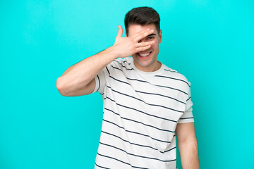 Young caucasian man isolated on blue background covering eyes by hands and smiling