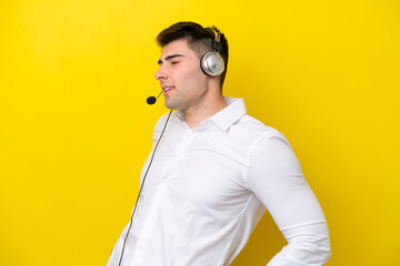 Telemarketer caucasian man working with a headset isolated on yellow background suffering from backache for having made an effort