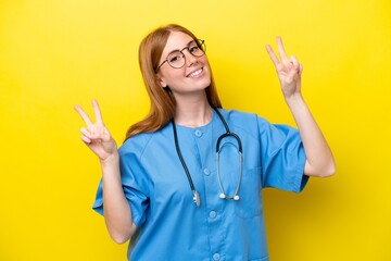Young redhead nurse woman isolated on yellow background showing victory sign with both hands