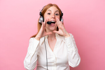 Telemarketer redhead woman working with a headset isolated on pink background shouting and...