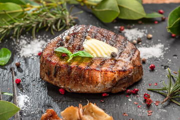 Grilled delicious ribeye steak with melting piece of butter on it. Steak is on black slate serving plate. Flat lay.