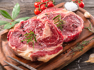 Raw beef steaks with herbs and spices ready for cooking are on wooden board.