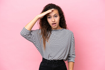 Young hispanic woman isolated on pink background doing surprise gesture while looking to the side