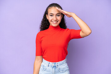 Young woman isolated on purple background saluting with hand with happy expression