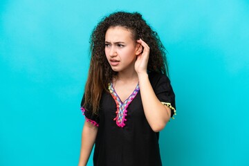 Young Arab woman isolated on blue background listening to something by putting hand on the ear