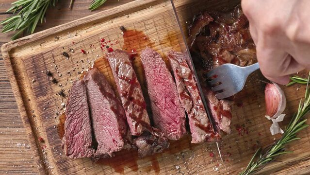 Chef slicing freshly grilled juicy beef steak meat with a knife on a wooden cutting board in the kitchen, food close-up