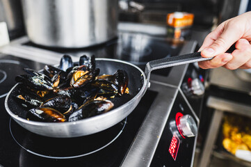 Close-up of a hand flipping mussels in a frying pan on a stove