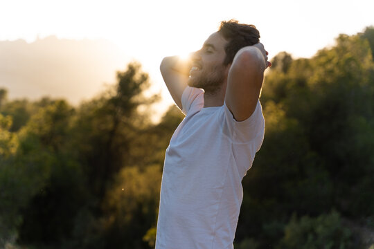 Attractive and smiling man in contact with nature breathing fresh air at sunset