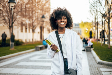 Beautiful and happy Black female student enjoying outdoors in college campus while study for the faculty exam.