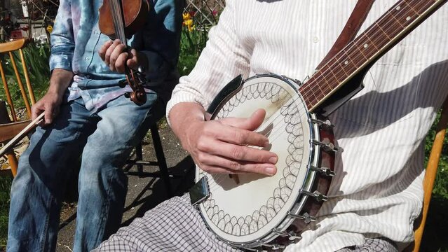 A musician plays the banjo accompanied by a violinist during a sunny day.