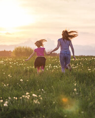 Mother and her little daughter running in the meadow into the sunset light.