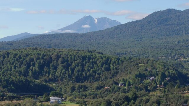 Aerial shot of dense green mountain forest with Calbuco Volcano in the background in southern Chile
