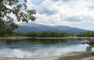 A tranquil lake unfolds against a mountainous backdrop, its waters placid beneath a cloud-filled sky