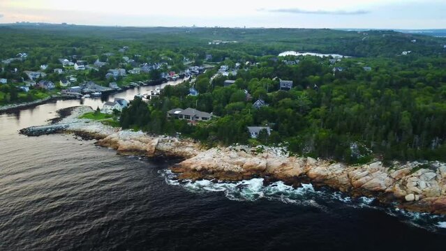 Drone shot of rocky sea cliffs by the ocean with a small coastal town in Nova Scotia.