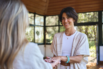 Happy female holistic teacher holding hands of woman during spiritual practice meditation...