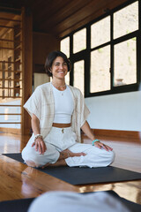 Young happy woman yoga coach instructor training group meditation yoga class sitting in yoga pose in studio talking to people during retreat mind body health therapy session. Vertical candid photo.