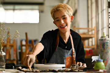 A smiling Young Asian boy enjoys making ceramics, working in an art workshop, LGBT people and...