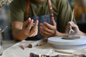 Close-up of an artist's hands shaping clay and using a sculpting tool on a pottery wheel. The image...
