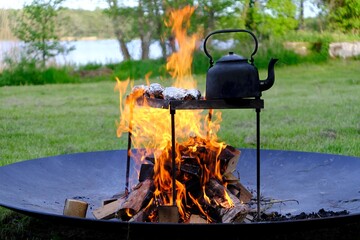 An old metal kettle stands among the flames of the fire. There's grilled food in aluminum foil....