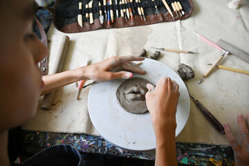 An artist's hands shape clay on a pottery wheel, surrounded by sculpting tools in a creative...