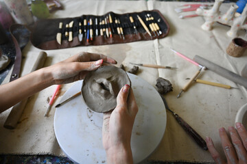 Close-up image of an artist's hands shaping clay on a pottery wheel, surrounded by sculpting tools...