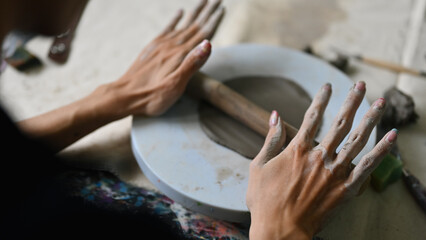 Close-up over-shoulder image of Young potter rolling out clay, Skillful Young artisan at work, rolling clay with a rolling pin