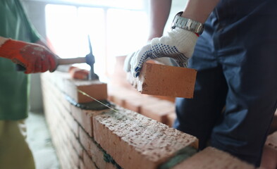 Male builder hand in gloves holding clay brick on background of brickwork wall. Repair and redevelopment apartments concept.