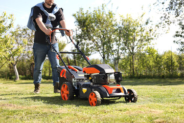 Man cutting green grass with lawn mower in garden, closeup
