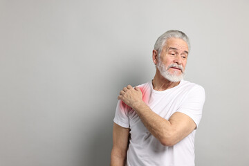 Senior man suffering from pain in shoulder on grey background. Space for text