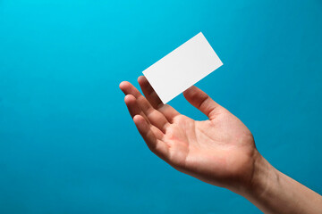 Man with blank business card on light blue background, closeup. Mockup for design