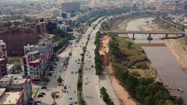 Drone view of traffic on roads between buildings and bridge with river on a sunny day in Bahria Town